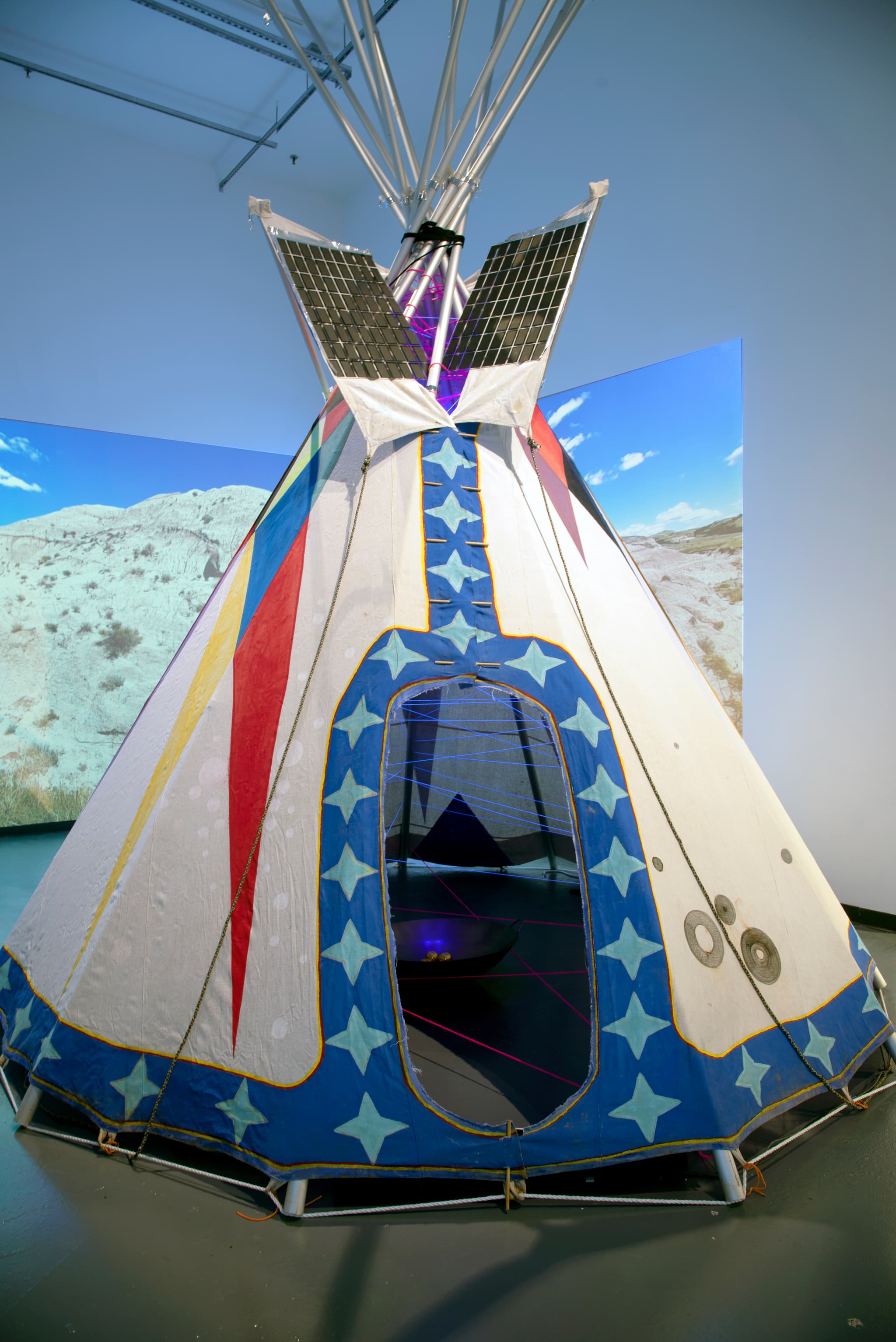 A large, colorful cloth tipi with collapsible metal support poles stands tall.
